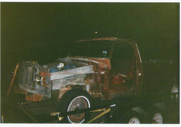 Stripped red truck body with front end removed, loaded on a trailer at night