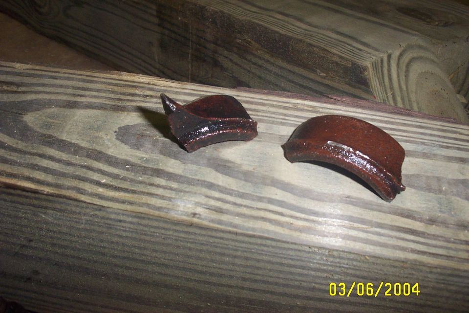 Two broken pieces of reddish-brown ceramic resting on wooden planks