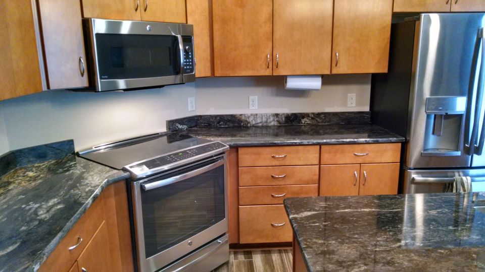Kitchen with stainless steel microwave, range, and refrigerator. Granite countertops and wood cabinets