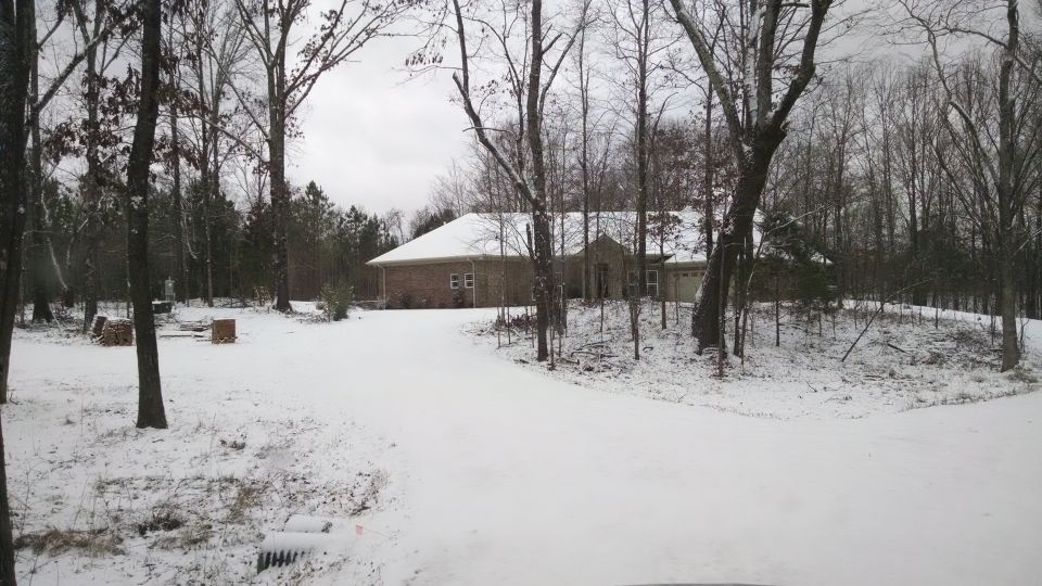 House with snow on the roof and ground, surrounded by bare trees