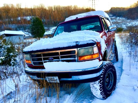 1995 Ford Bronco - A red Ford Bronco sits partially buried in snow on a winter day, its tires deep in the snow-covered ground.
