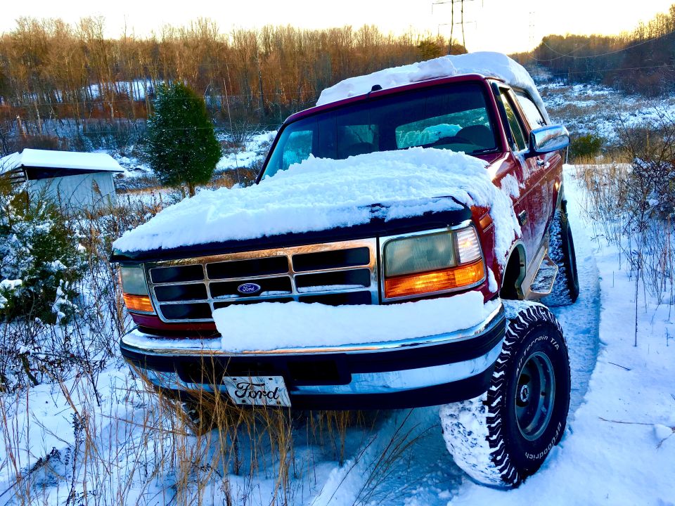 Red Ford Bronco covered in snow, front 3/4 view, parked on a snowy path