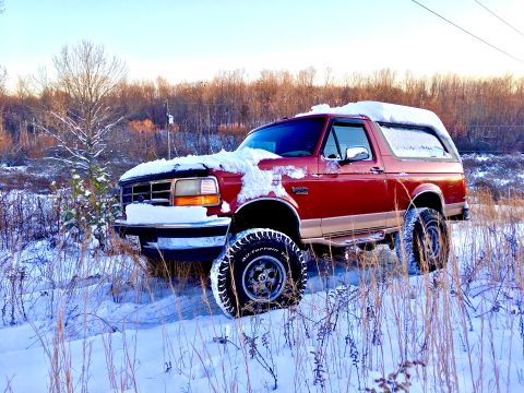 1995 Ford Bronco - A red 1995 Ford Bronco is parked in a snowy field with trees in the background.