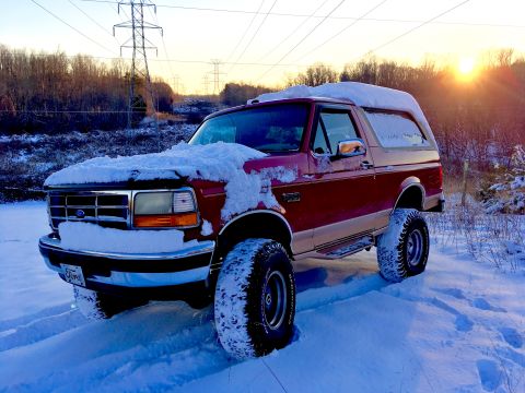 1995 Ford Bronco - A 1995 Ford Bronco sits in a snowy landscape as the sun sets behind it.