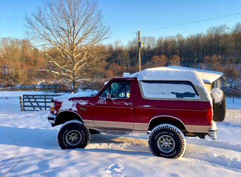 1995 Ford Bronco - A red Ford Bronco sits in a snowy landscape, its body partially covered by snow.