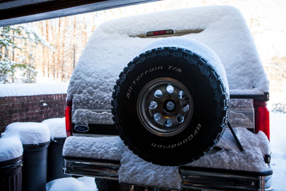 Rear view of a 1995 Ford Bronco covered in snow, parked outside