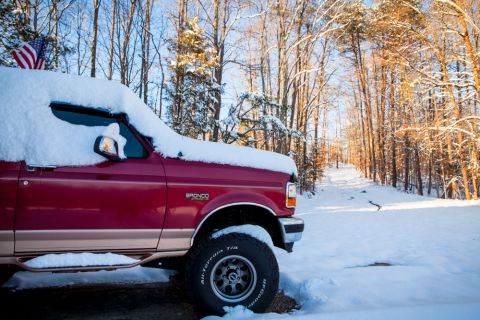1995 Ford Bronco - A red 1995 Ford Bronco sits covered in snow, ready for winter fun, with an American flag flying proudly.