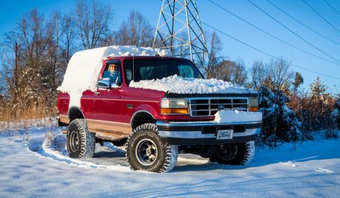 1995 Ford Bronco - A red Ford pickup truck is covered in snow, suggesting it has been driven or parked in a winter storm.