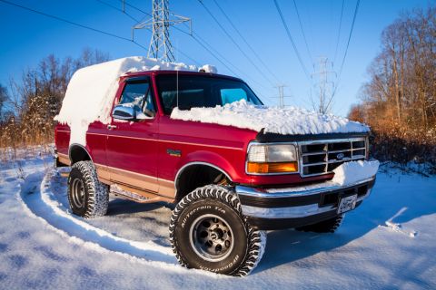 1995 Ford Bronco - A red Ford Bronco navigates a snowy path, its body partially obscured by winter snow.