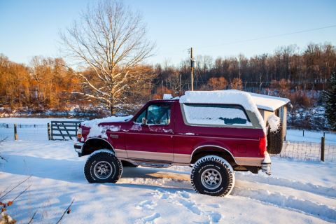 1995 Ford Bronco - A red 1995 Ford Bronco sits covered in snow on a bright winter day.