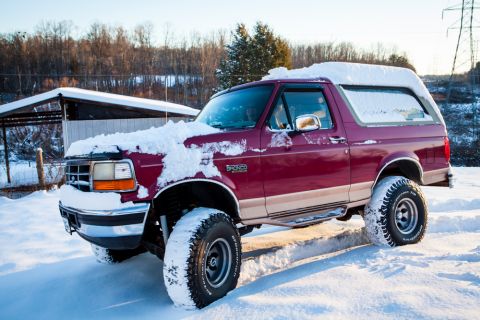 1995 Ford Bronco - A red 1995 Ford Bronco sits covered in snow on a bright winter day.