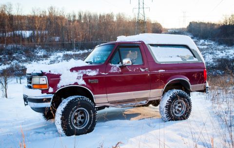 1995 Ford Bronco - Maroon 1995 Ford Bronco with snow on its roof and hood, tires deep in snow.
