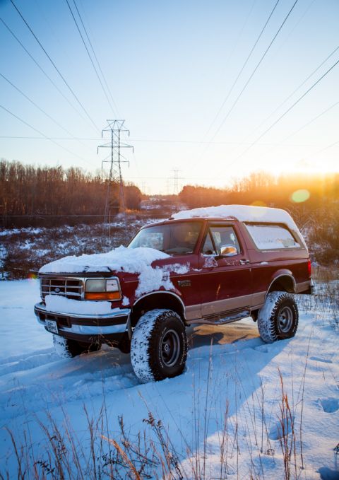 1995 Ford Bronco - A 1995 Ford Bronco is shown in a snowy landscape during sunset, with power lines visible against the sky.