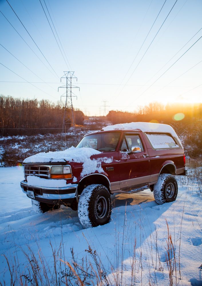 Maroon Ford Bronco with snow on it, driving in a snowy field with power lines overhead