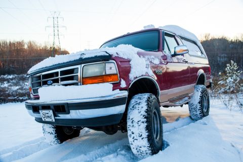 1995 Ford Bronco - A red 1995 Ford Bronco navigates a snowy landscape, its tires deep in the snow.