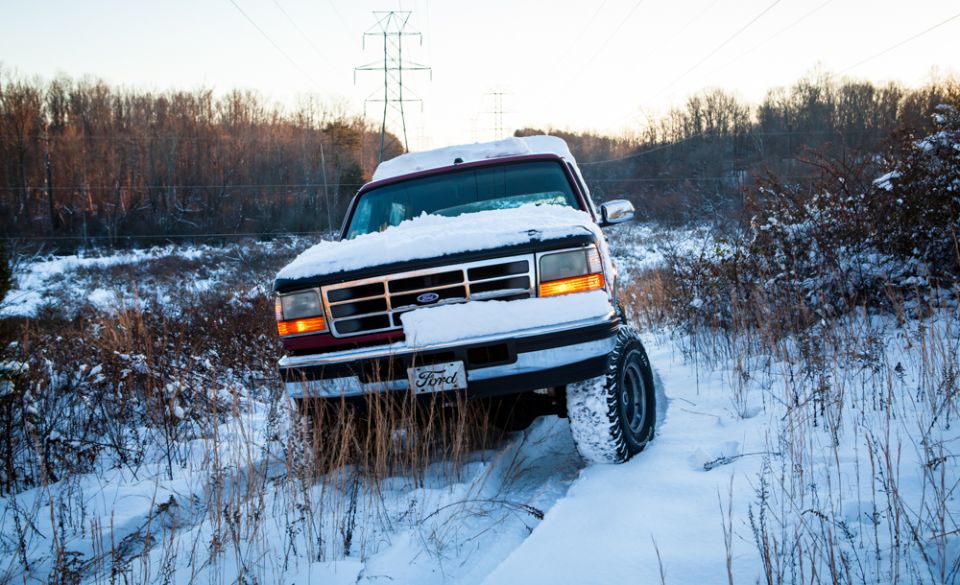 Ford truck with snow on hood driving through a snowy path with trees and power lines in background
