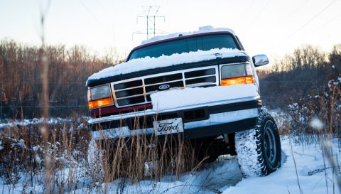 1995 Ford Bronco - A 1995 Ford Bronco navigates a snowy landscape, its front grille and headlights visible under a blanket of snow.
