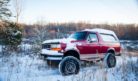 1995 Ford Bronco - A red 1995 Ford Bronco sits partially covered in snow during a winter day.