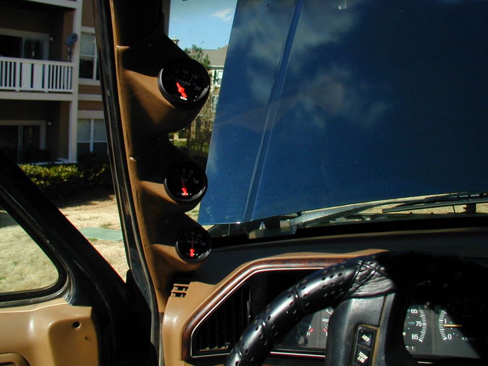 Dashboard with three gauges mounted on the A-pillar, a leather-wrapped steering wheel, and part of the dashboard. The hood is open