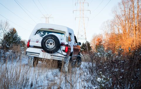 1995 Ford Bronco - A white Ford Bronco navigates a snowy, off-road path under power lines.