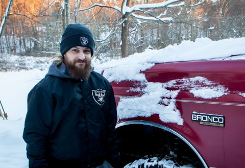 1995 Ford Bronco - A man in a Raiders jacket stands beside a red Ford Bronco covered in snow during winter.