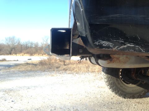 1979 Ford Bronco - A custom hitch receiver is attached to the rear of a black SUV, showing the tire and suspension components.