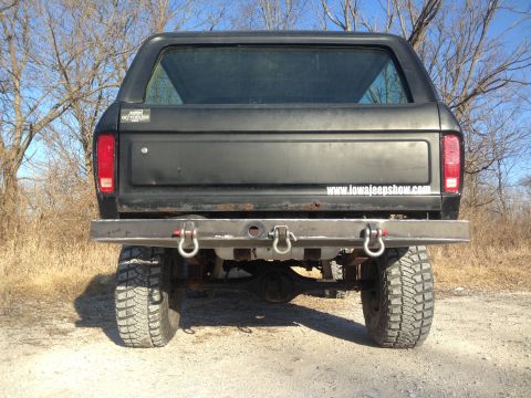 1979 Ford Bronco - Rear view of a black SUV with a custom bumper and off-road tires, a website sticker on the tailgate.