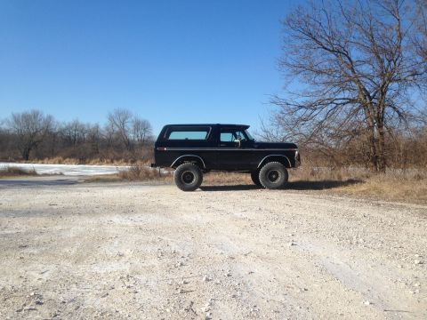 1979 Ford Bronco - Side view of a black Ford Bronco parked on a dirt road with bare trees and a frozen body of water in the background.