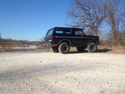 1979 Ford Bronco - A black Ford Bronco is parked on a gravel road with a winter landscape behind it.