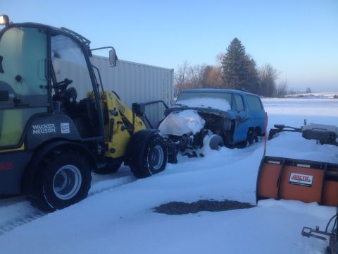 1979 Ford Bronco - A blue SUV, partially covered in snow, is being moved by a loader in a snowy outdoor scene.