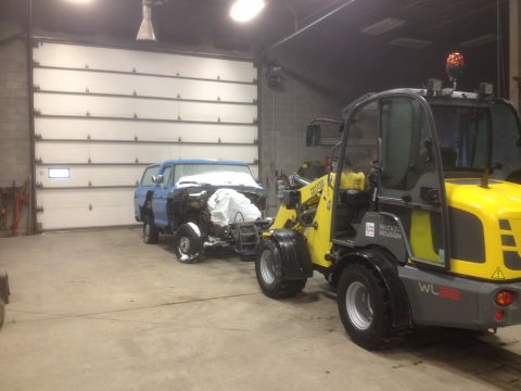 1979 Ford Bronco - A blue pickup truck, partially disassembled and covered in snow, is being towed by a yellow loader in a garage.