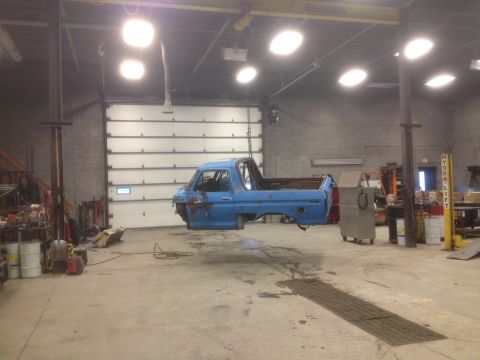 1979 Ford Bronco - A blue pickup truck body is being worked on in a garage, suspended by a hoist.