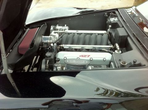 1976 Chevrolet Corvette - The engine bay of a black car is shown with a prominent "427" engine badge and a red air filter.