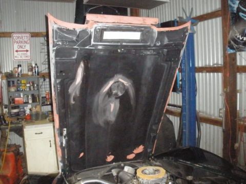 1976 Chevrolet Corvette - The underside of a car hood reveals primer and engine parts, with a sign indicating 'Corvette Parking Only'.