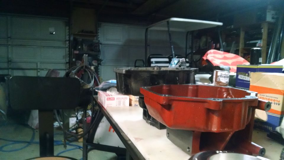 Red and black automotive oil pans on a workbench in a garage with a golf cart in the background