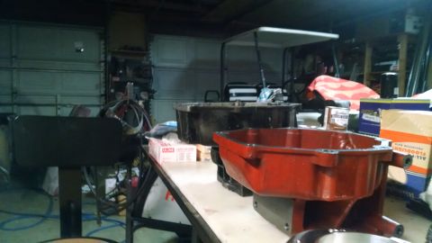 1985 Jeep CJ7 - Automotive parts, likely oil pans, are laid out on a workbench in a cluttered garage setting.