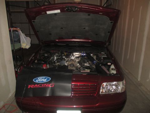2004 Ford Crown Victoria - The engine bay of a red 2004 Ford Crown Victoria is visible with the hood open, a Ford Racing fender cover.