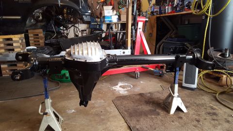 1994 Ford Bronco - The rear axle assembly of a Ford Bronco is shown on jack stands, undergoing restoration in a workshop.