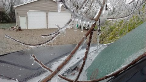 1985 Ford Bronco - Branches coated in ice obscure the view of a car windshield and a garage during a winter storm.