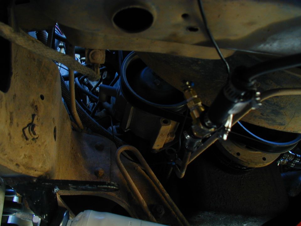 Engine bay with hoses and metal components. A brass fitting connects to a black hose
