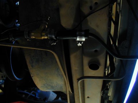 1988 Ford Bronco - Close-up view of a modified fuel line under a vehicle, a brass T-fitting and hose clamps.
