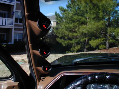 1988 Ford Bronco - Three gauges are mounted on the A-pillar of a vehicle, with an outdoor scene visible through the windshield.
