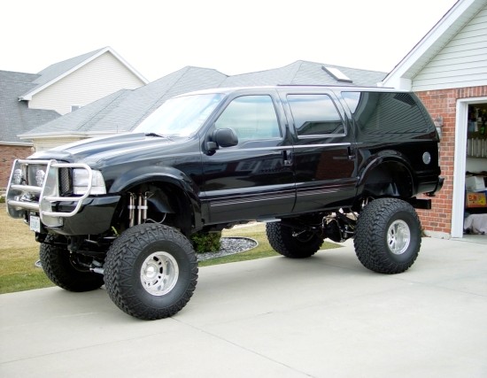 Lifted black Ford Excursion SUV on oversized tires parked in a driveway.