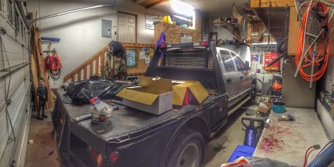2004 Dodge 3500 - A silver flatbed truck is parked inside a garage filled with tools and storage items.