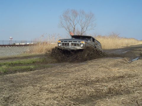 1979 Ford Bronco - A Ford Bronco navigates a muddy terrain, kicking up a large spray of mud.