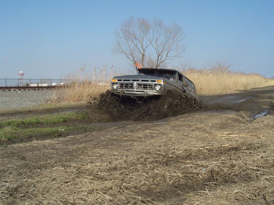Dark gray 1978 Ford Bronco driving through mud, front grille visible