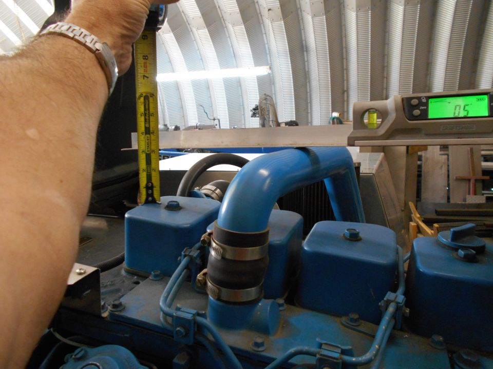hand holding tape measure over blue engine component, digital level shows 0.5