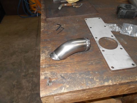 1992 Ford Bronco - Metal exhaust pipe and mounting plate on a workbench, with tools and other items in the background.