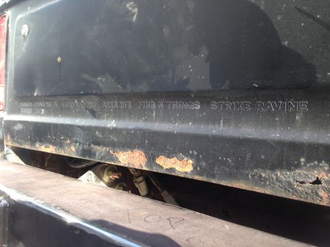 1979 Ford Bronco - Close-up of the rear panel of a vehicle, showing embossed text and significant rust damage along the lower edge.