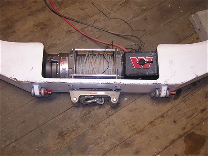 1993 Ford Bronco - A winch is mounted to a white bumper assembly, with red tow hooks on either side.